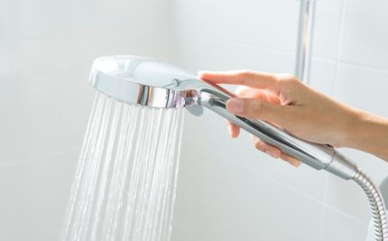 Hand holding a shower head away from shower walls concept image for shower waterproofing