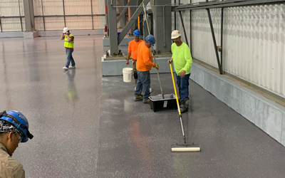 Workers applying floor coating with abrasion resistance on concrete floors inside the commercial property.