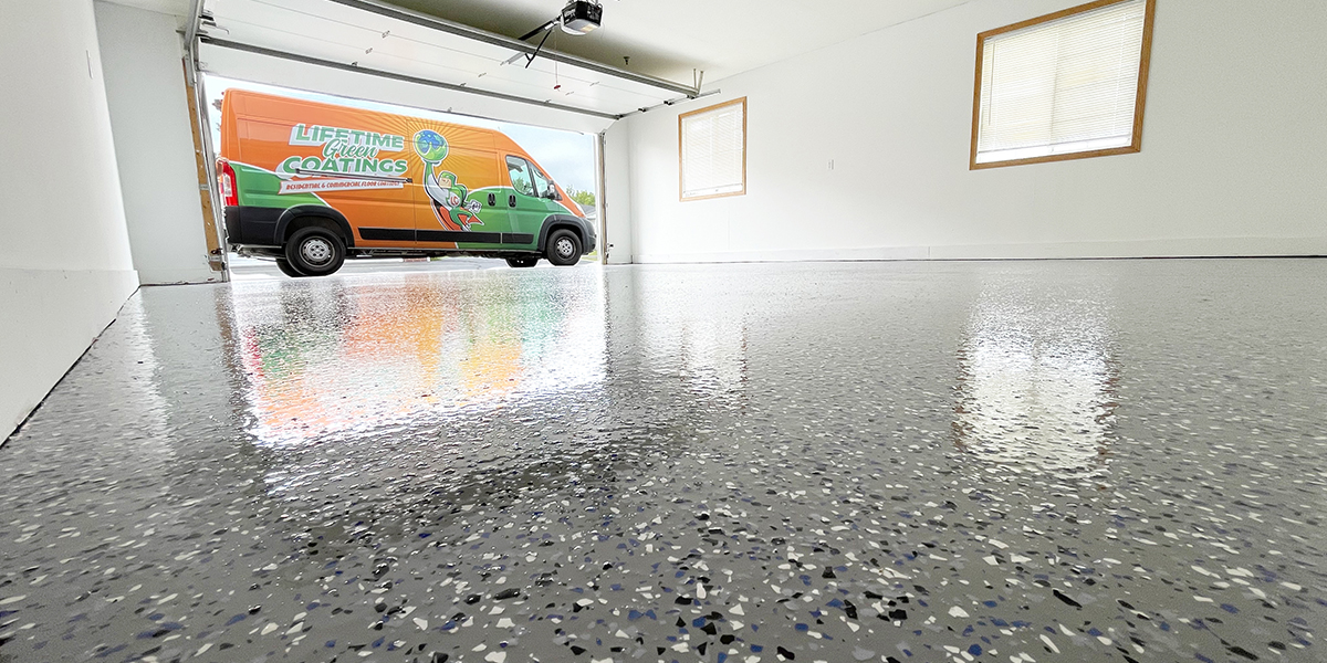 Newly coated garage floor with decorative flakes and a polished finish, featuring a Lifetime Green Coatings van parked outside.